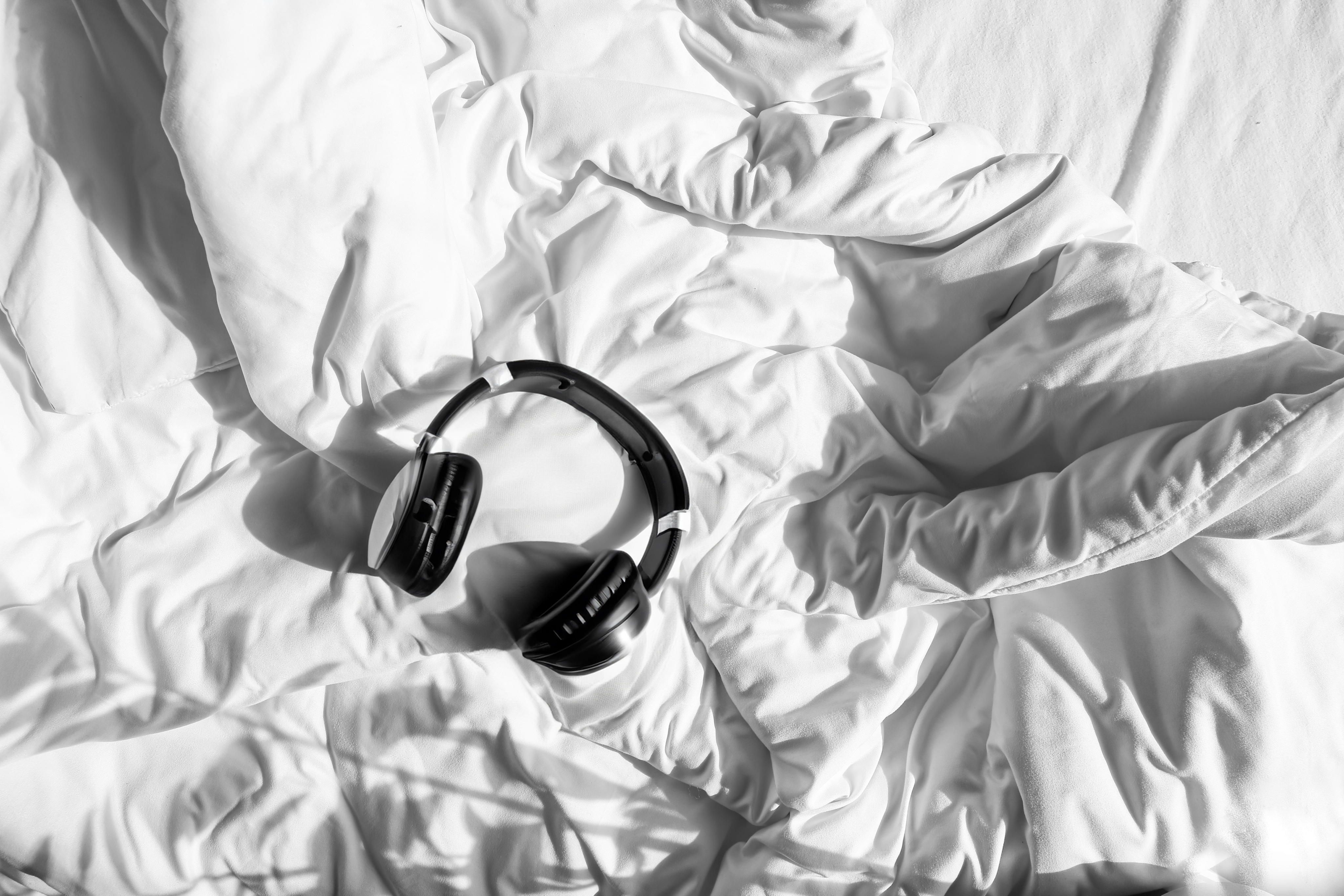 Black headphones resting on a crumpled white comforter under the bright Nashville light.