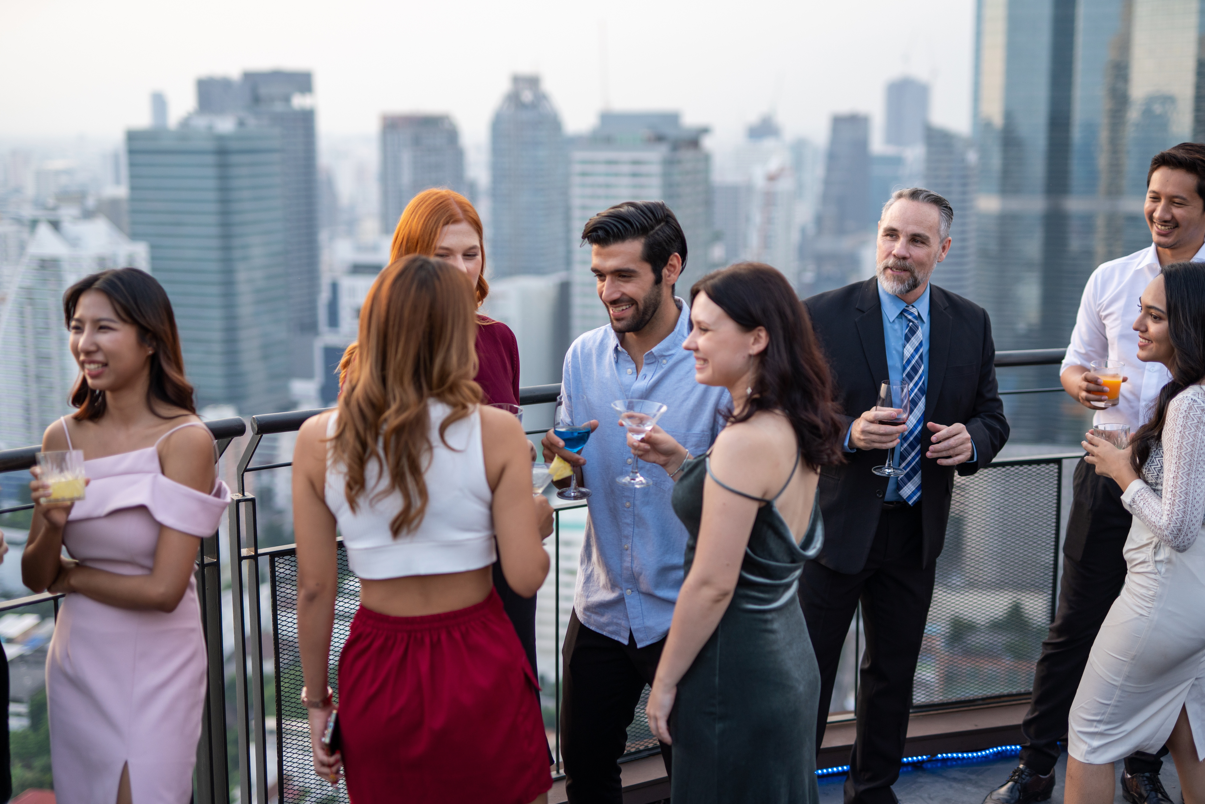 A group of people socializing on a Nashville rooftop with a stunning city skyline in the background. Some are holding drinks.