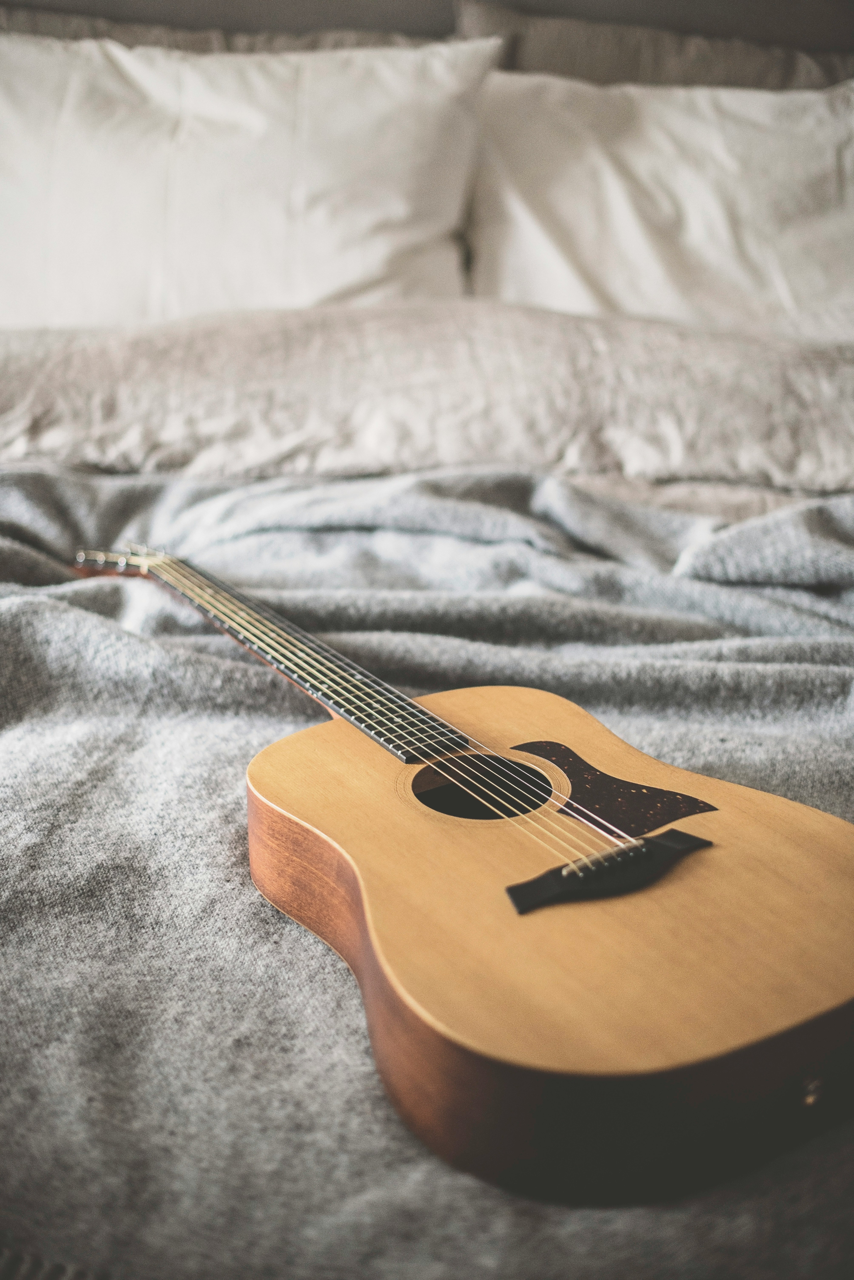 An acoustic guitar rests on a gray blanket-covered bed with white pillows, evoking the soulful spirit of Nashville.