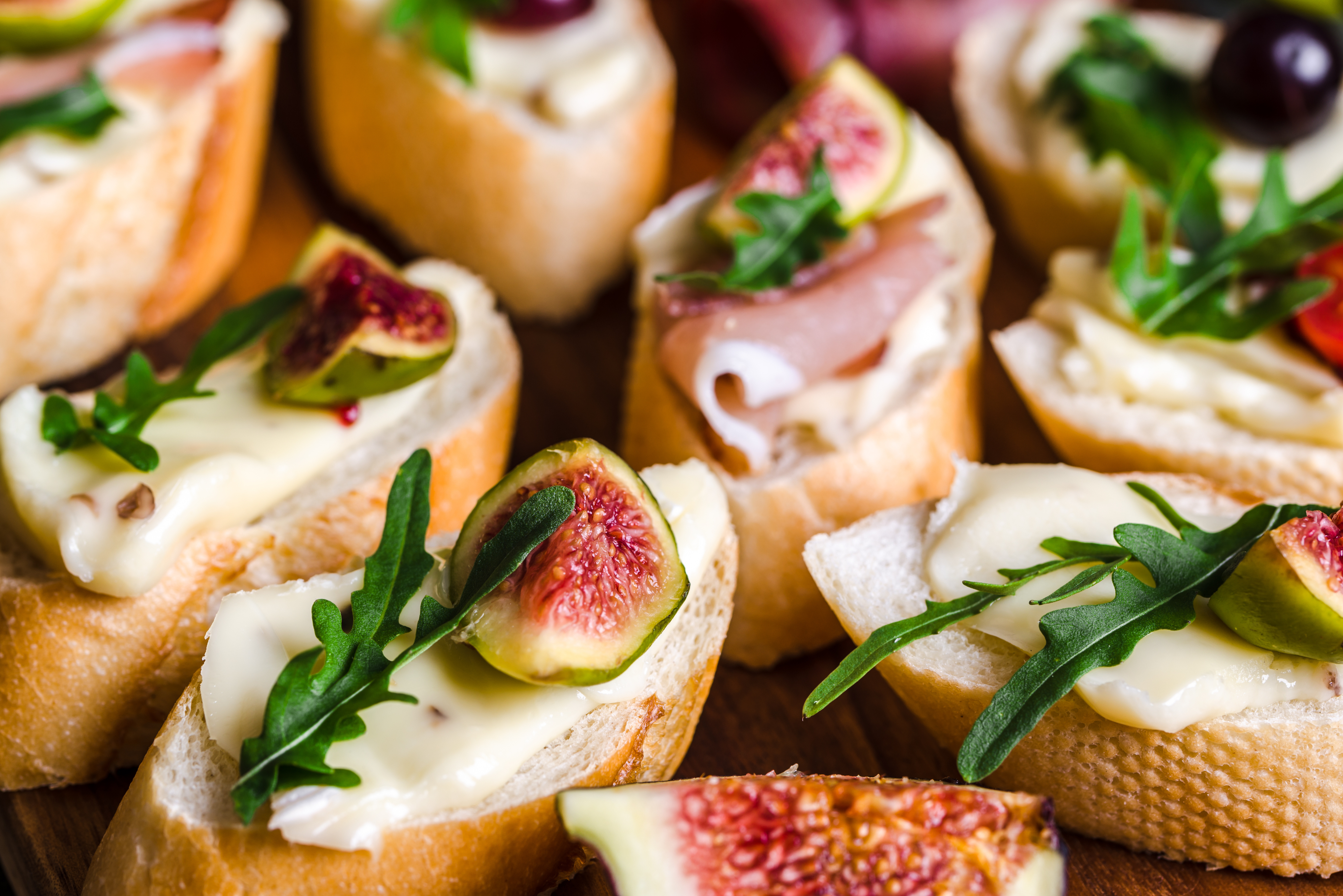 Close-up of assorted baguette slices topped with Nashville flair: creamy cheese, ripe figs, savory prosciutto, fresh arugula, and juicy grapes.