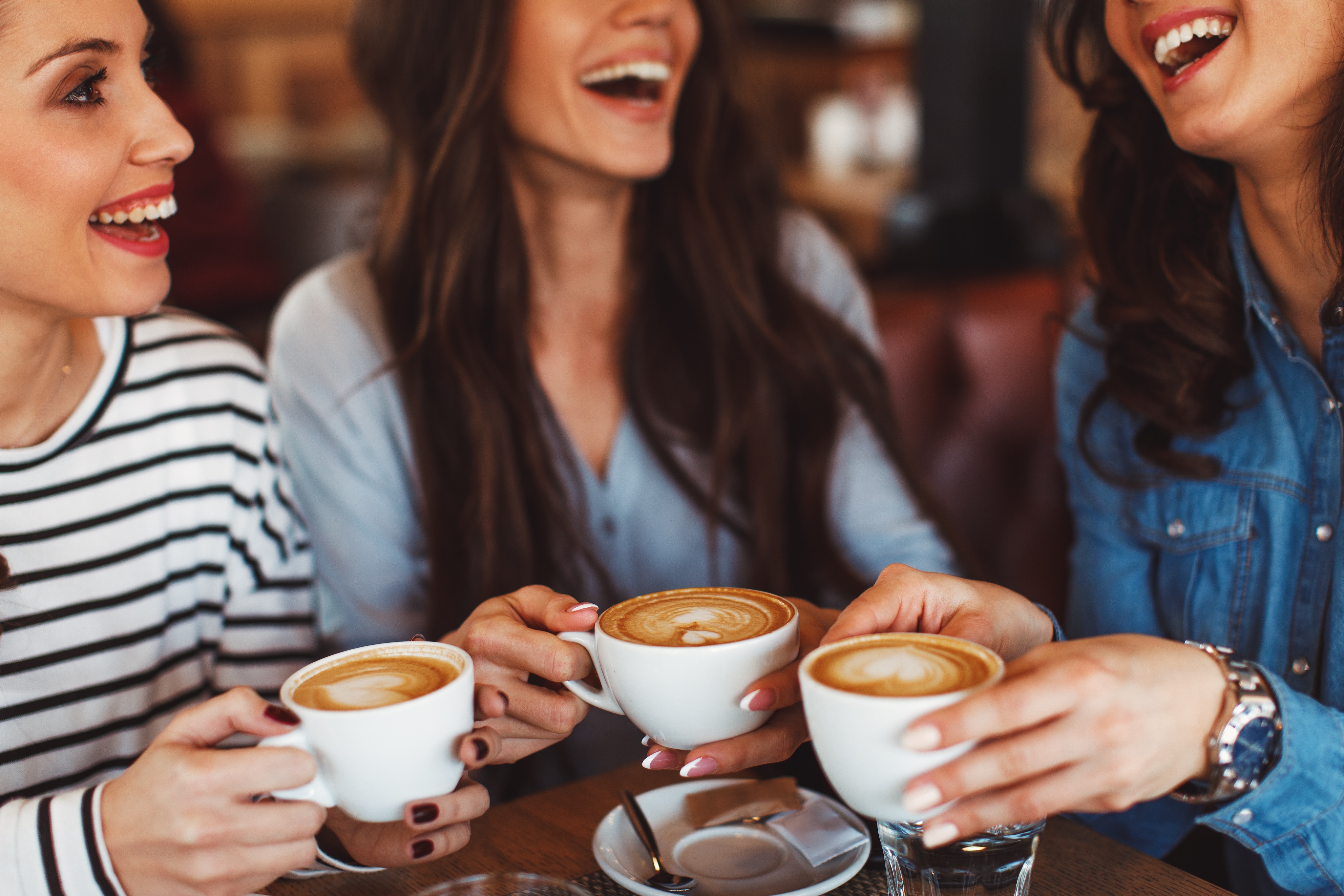 Three people at a cozy Nashville café, smiling and holding latte cups adorned with intricate latte art.