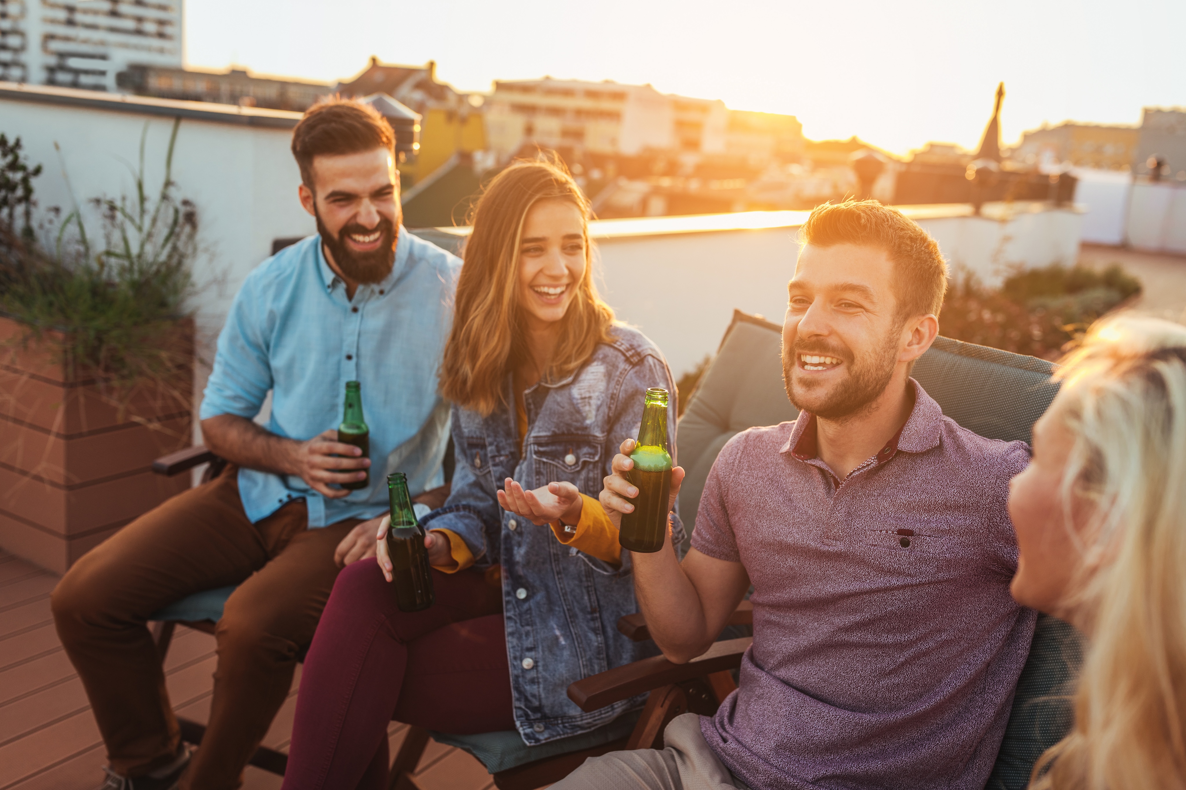 Four people are sitting on a charming Nashville rooftop terrace, holding drinks and chatting as the sun sets in the background.