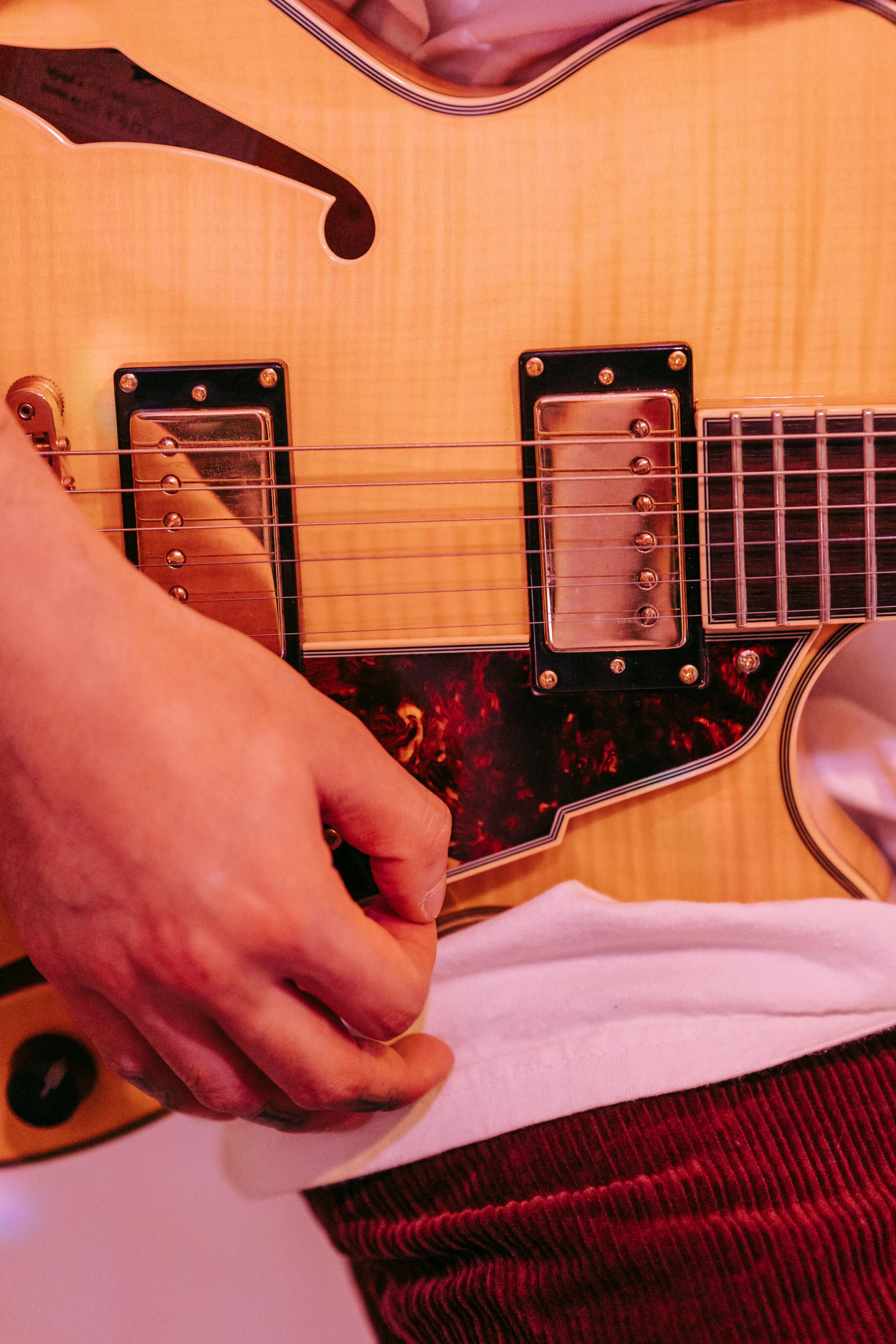 Close-up of a person playing a wooden electric guitar, focusing on the hand strumming and the guitar body, echoing the soulful sounds of Nashville.