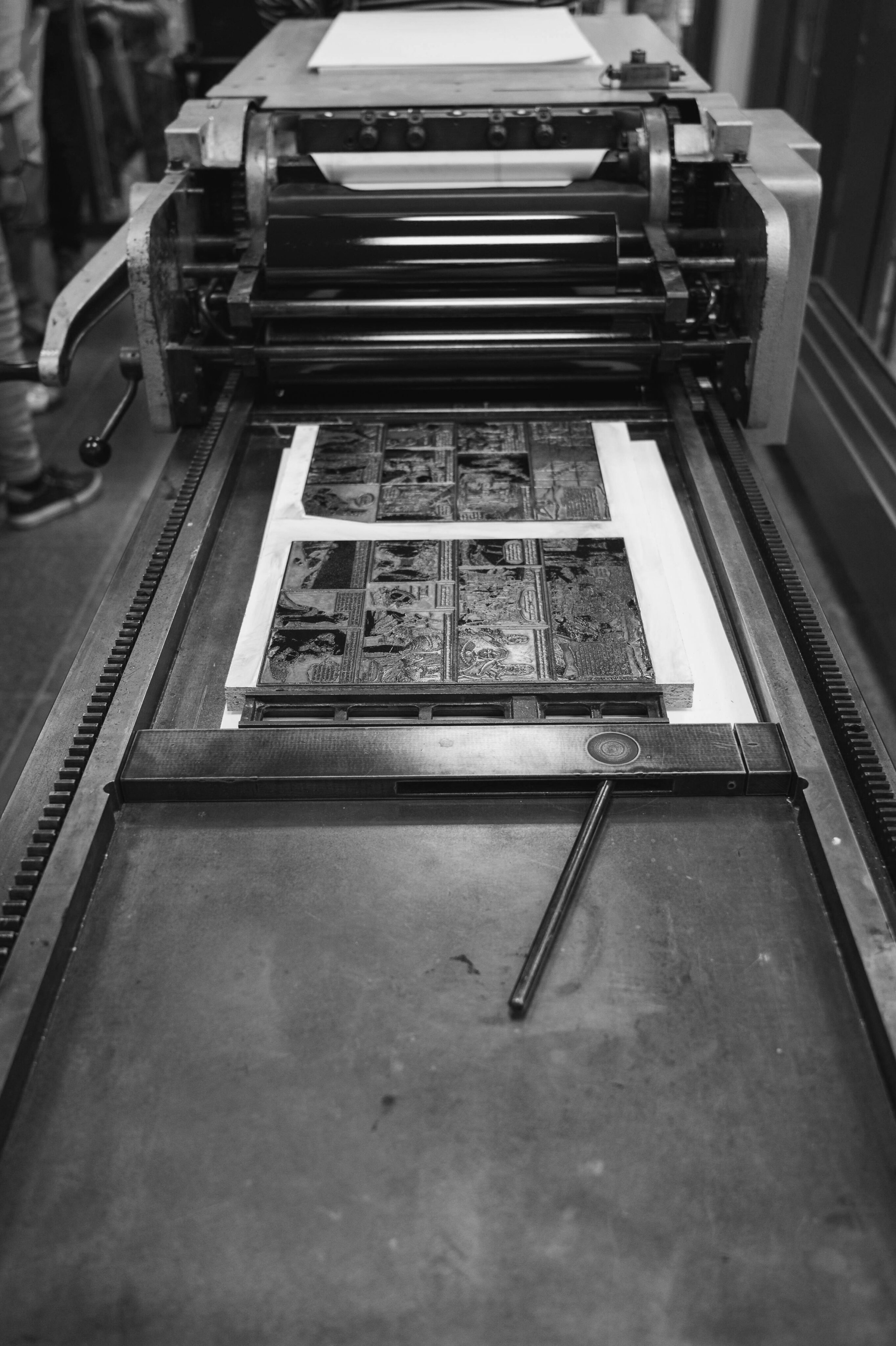 Black and white image of an old printing press in a Nashville print shop, with inked plates and rollers, showcasing a mechanical process.