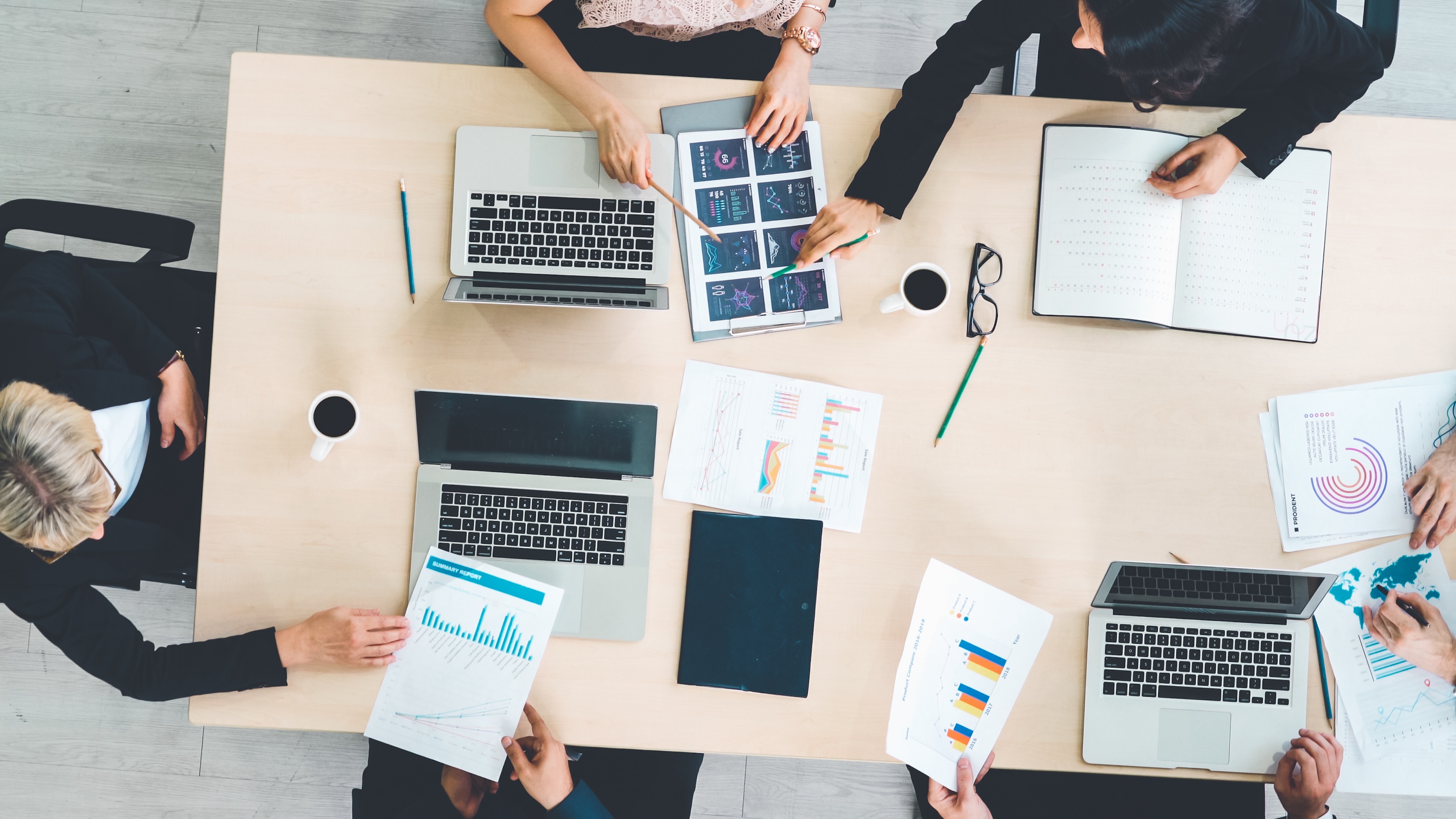 Aerial view of a Nashville business meeting with six people, laptops, charts, and coffee cups adorning the table.