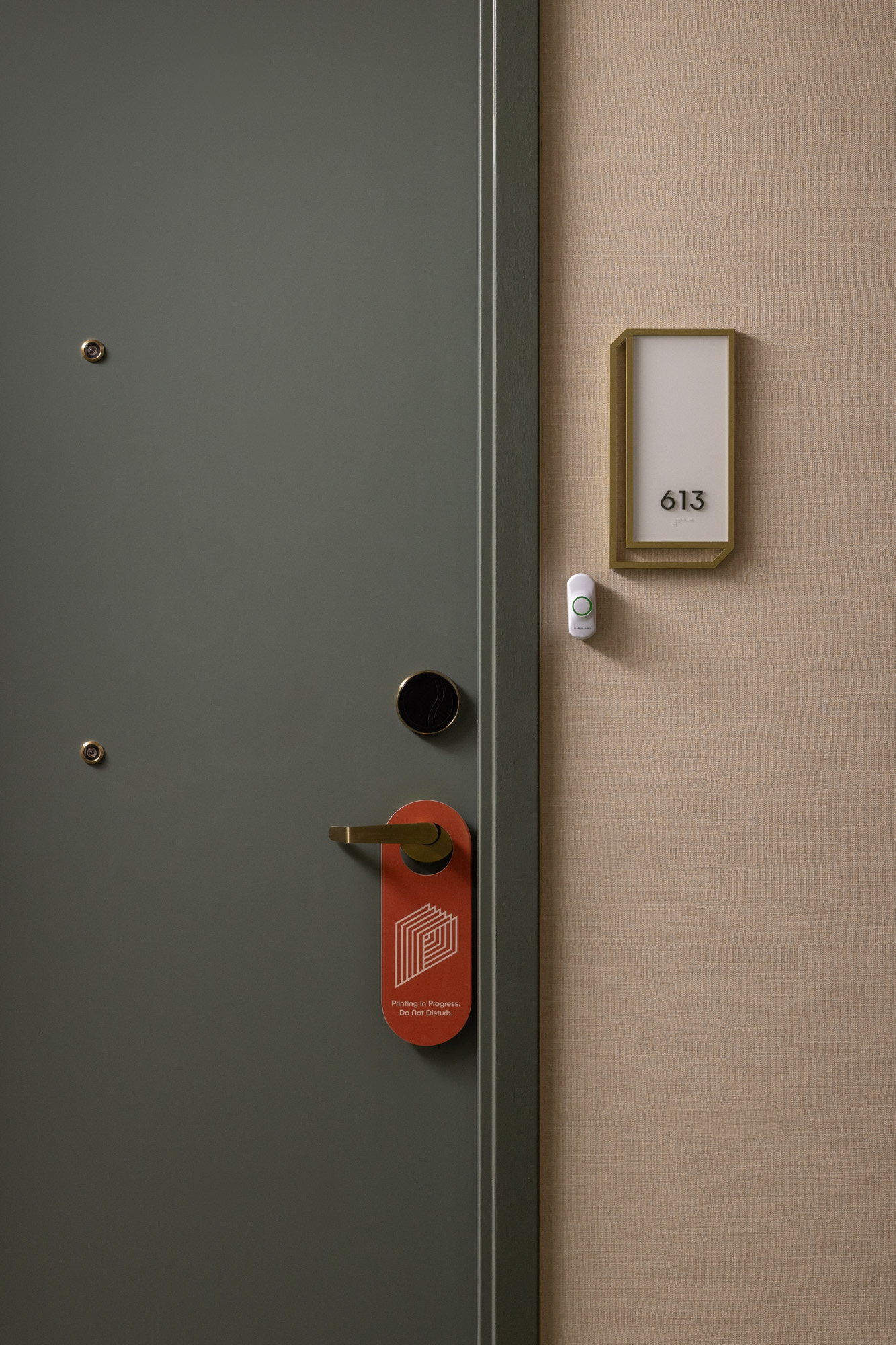 A closed green door with a gold handle, a red do not disturb sign, a peephole, and a room number sign reading 613 on a beige wall.