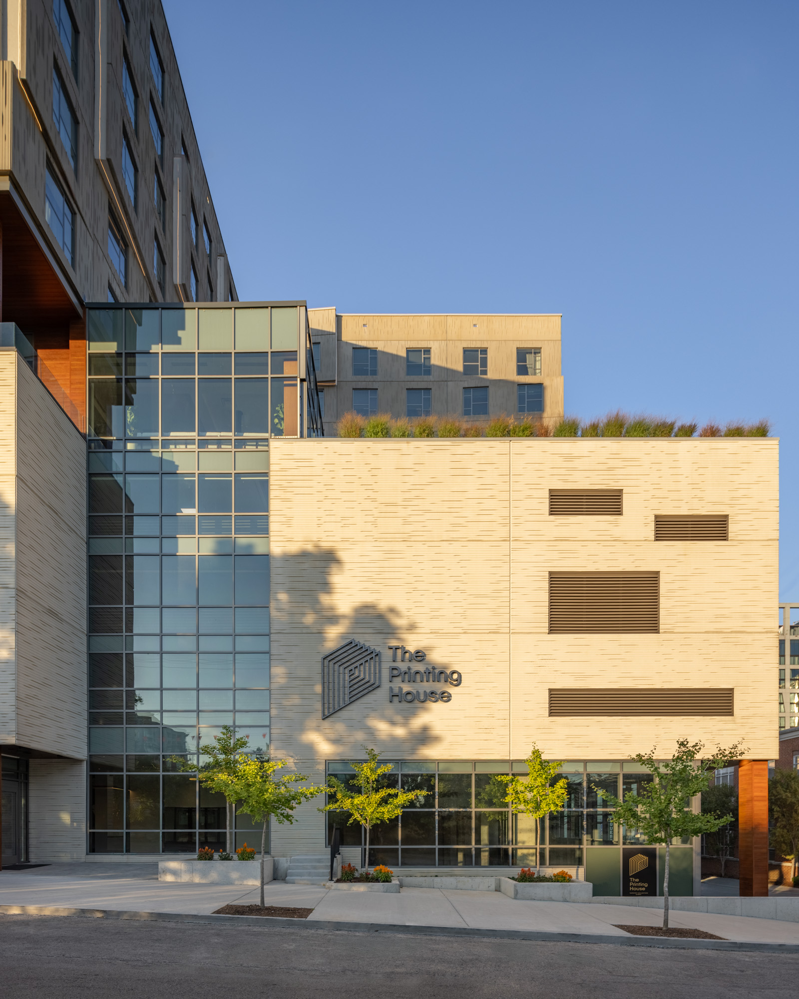 Modern multi-story building with large windows and "The Printing House" sign on the facade; small trees line the sidewalk in front.