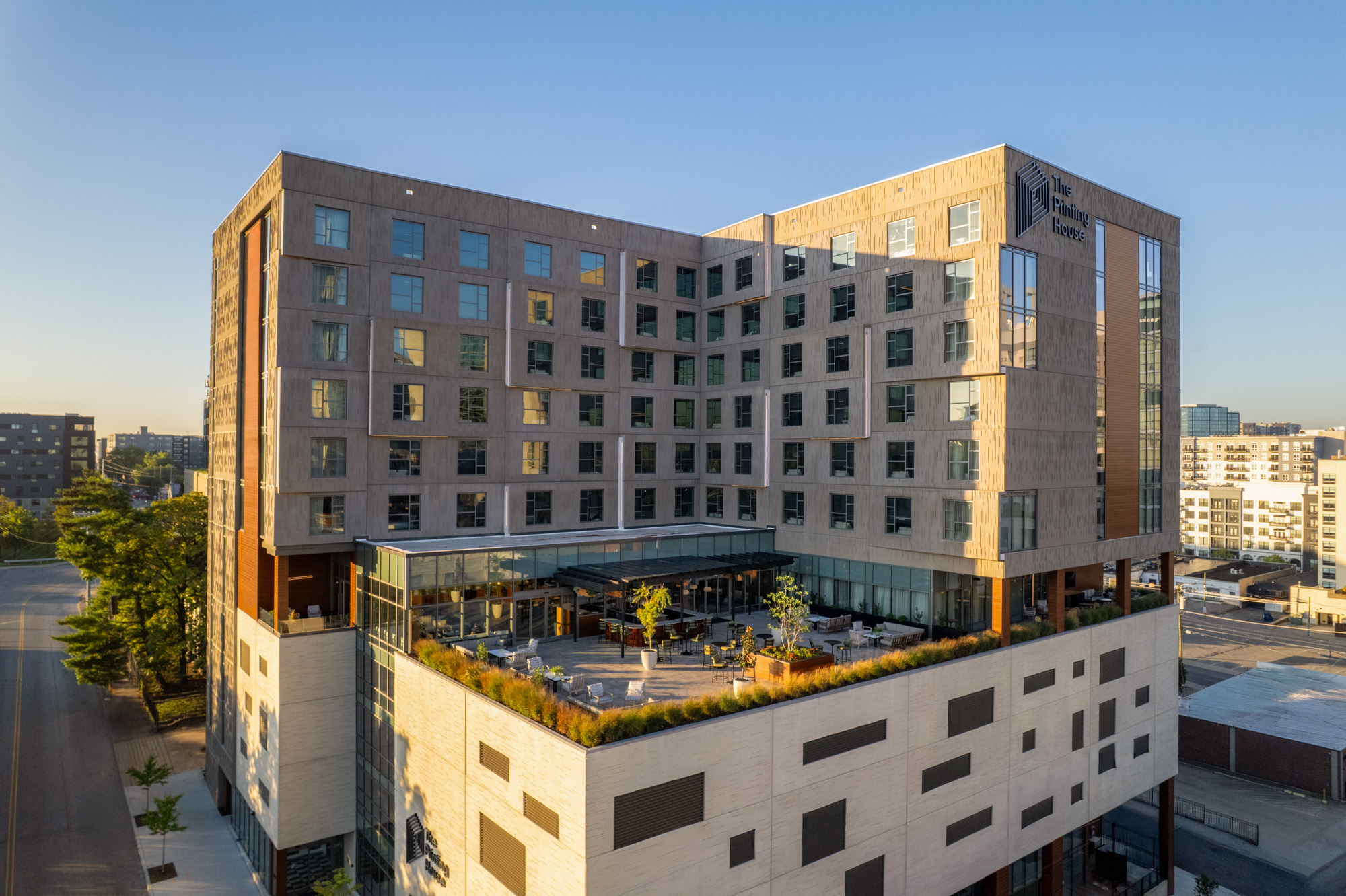 A modern multi-story hotel building with large windows and an elevated outdoor terrace, set against a clear sky in an urban area.